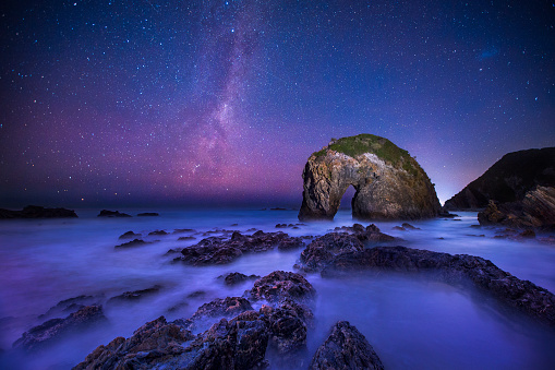 Milky way galaxy at night with unique rock formation of a horse drinking water in foreground. Shot at Horsehead Rock, South Coast, Australia.