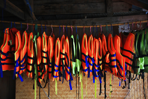 Orange life vest jackets hanging on rack outdoor for safety and protection while using in as swimming at the sea.