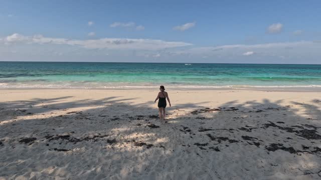 Woman traveler walks towards beach, crystal clear blue water