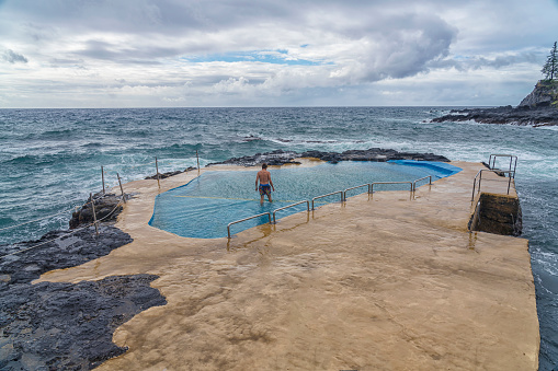 One men swimming in natural hot spa in the middle of the sea, volcanic coast. Sao Miguel, Azores