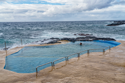 One men swimming in natural hot spa in the middle of the sea, volcanic coast. Sao Miguel, Azores