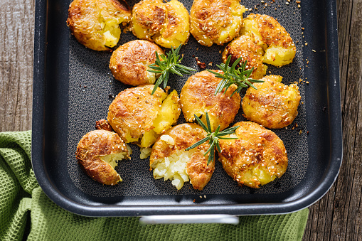 Baked or roast potatoes in metal baking tray seasoned with rosemary and salt and pepper. Golden and crispy. Cooking process on wooden rustic board