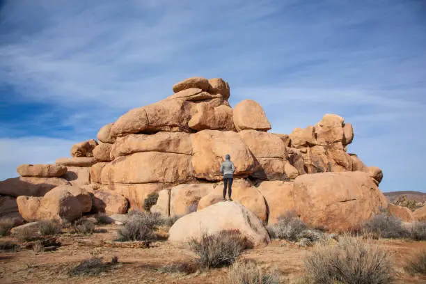 Woman standing and admiring the  the dramatic giant boulders in Joshua Tree National Park