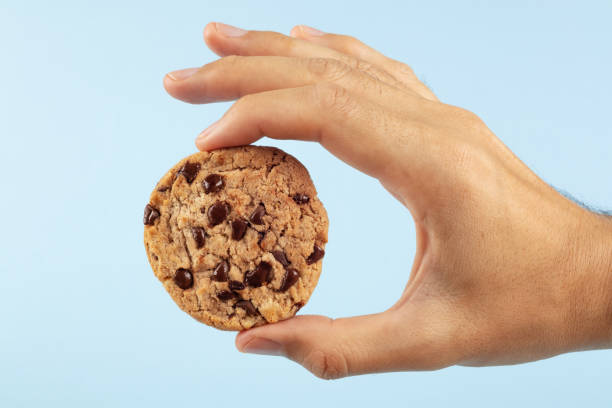 istock Man's hand holding a chocolate chip cookie on a blue background. 1495913509