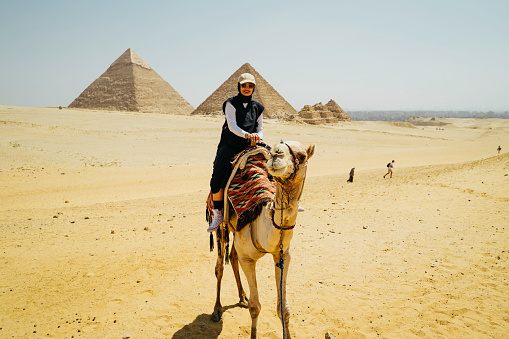 Egypt, Cairo, asian female tourist riding camel with Great Pyramid of Giza in background