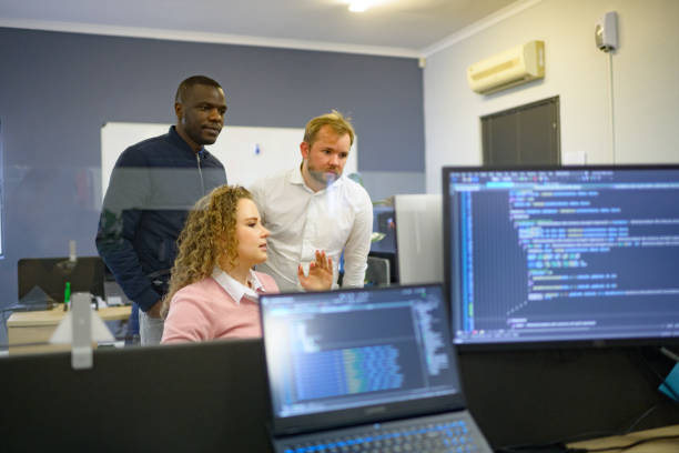 istock Multiracial Male and Female Group of Computer scientists discussing work with colleagues in an office with code and screens 1495914197