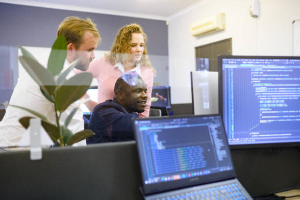 istock Low Side view Multiracial Group of Computer scientists discussing work with colleagues in an office with code and screens 1495914883