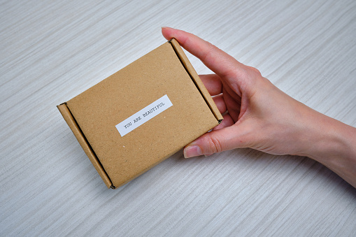Woman is holding a small paper box in her hand. A young girl with a new package. Cardboard. Gift box, gift. Box close-up. Empty packaging, empty space. Cardboard case. You are beautiful