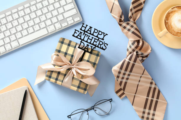Happy Father's Day concept. Vintage gift box, tie, glasses, keyboard, coffee cup, paper notebooks on light blue background. Flat lay, top view.