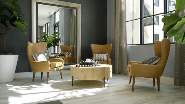 Stylish living room furnished with three yellow chairs with cushions, wooden coffee table and big mirror on dark grey wall. Tropical greenery in pots. Sunlight coming from windows