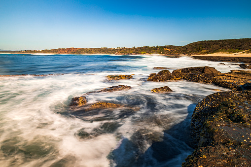 Waves washing over rocky coastal environment at the beach. Photographed in Australia.