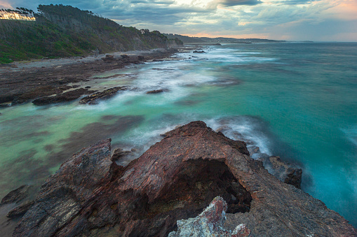 Long exposure of smooth ocean waves rolling into beach, photographed on the south coast of NSW, Australia.