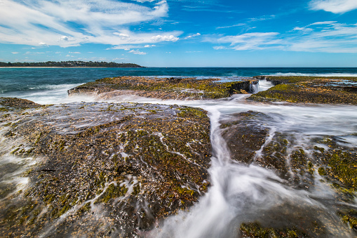 Seascape of water waves flowing over rocks at the beach on a perfect, clear sunny day. Photographed in Australia.