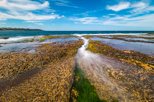 Seascape of water waves flowing over rocks at the beach on a perfect, clear sunny day. Photographed in Australia.