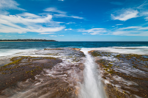 Seascape of water waves flowing over rocks at the beach on a perfect, clear sunny day. Photographed in Australia.