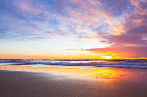 Seascape of golden sunset reflecting on the wet sand at low tide on the South coast of NSW, Australia.
