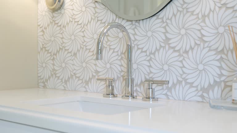 Close up of marble counter with clean wash basin and modern style faucet. White flowers on tiles and aroma diffuser standing near