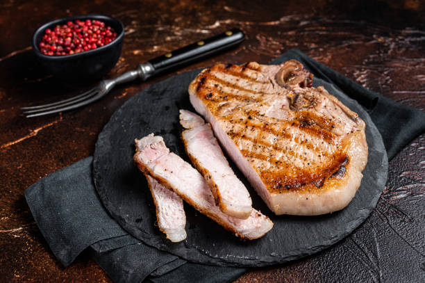 istock Roast BBQ pork Chop or T-bone meat steak sliced on a board. Dark background. Top view 1495926360