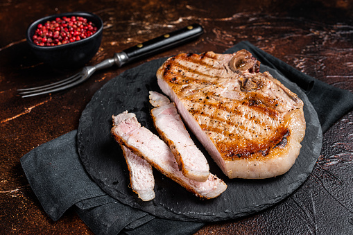 Roast BBQ pork Chop or T-bone meat steak sliced on a board. Dark background. Top view.