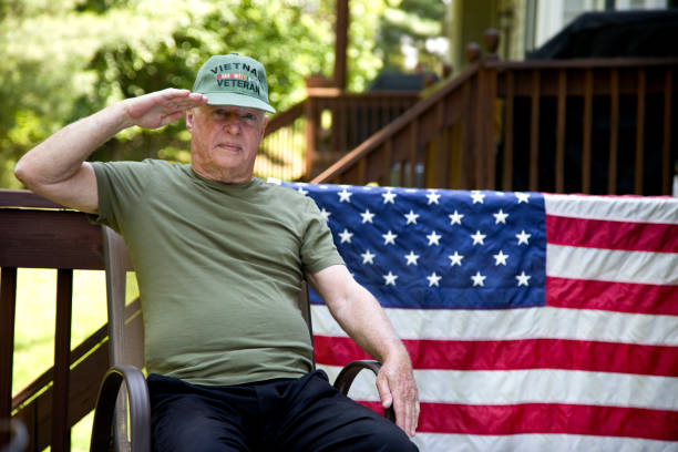 istock Vietnam Veteran sitting wearing cap looking at camera saluting 1495932734