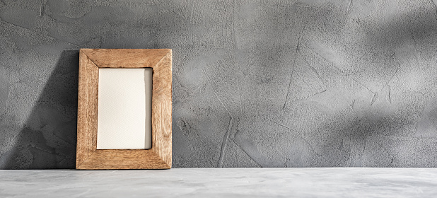 Mockup of an empty small wooden photo frame standing on a gray concrete table in sunlight. Copy space or photo space in a wooden frame.