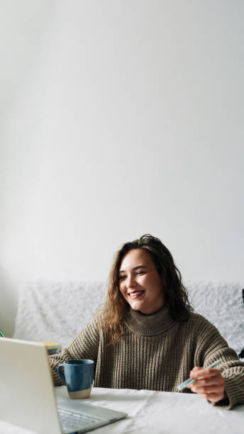 istock Successful female CEO multitasking at kitchen table during video conference with partners, using laptop, phone, and coffee cup 1495936625