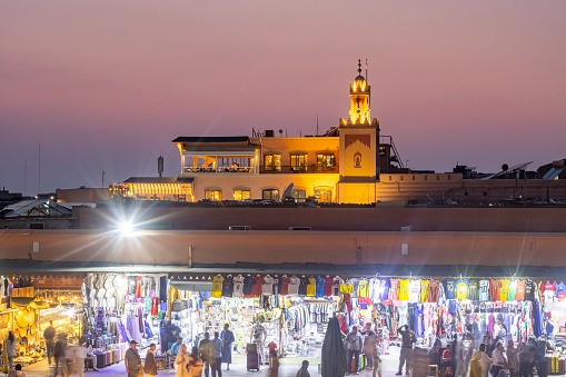 People are visible walking around Djemma el Fna Square in Marrakesh, Morocco, at dusk.