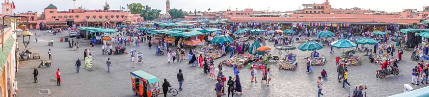 Djemma el Fna Square at Medina District in Marrakesh, Morocco, with many people, stalls and shops visible.