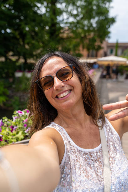 beautiful middle aged woman takes a selfie outdoors on a lakeside terrace stock photo