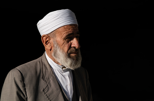 Portrait of imam who is a muslim cleric. long-bearded imam wearing a white turban. partial light portrait shot on a sunny day. Shot with a full-frame camera in daylight.