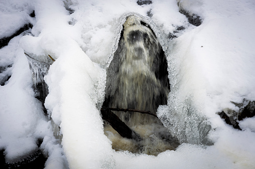 Winter wonderland with river and icy surrounding framed by a flowing creek, long exposure that bring forward a creature looking shape in water