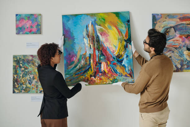 Couple of employees preparing for art exhibition Couple of employees hanging paintings on the wall, they preparing for art exhibition in gallery hanging art on wall stock pictures, royalty-free photos & images