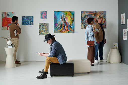 Group of people visiting gallery of modern art, they watching colorful paintings on the wall