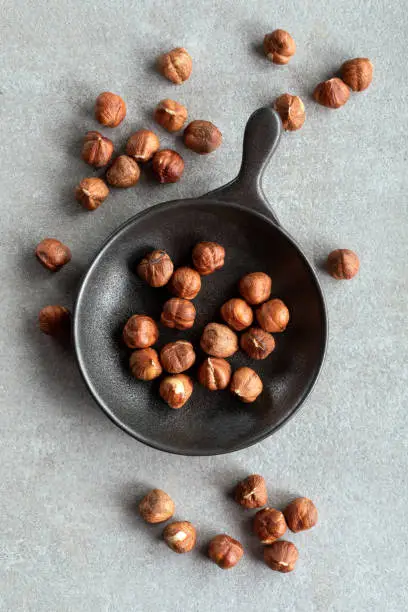 Photo of Fresh hazelnuts in black pan in black cup on stone background.