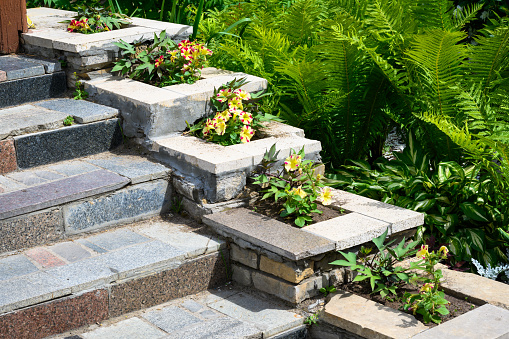 Landscaping on house stairway with flowerbeds, home landscape design. Upscale garden in summer. Flowers and plants on nice floral terraces in landscaped yard.