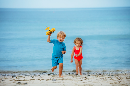 Little boy with sister girl run holding toy model of the plane over calm ocean and beach on background