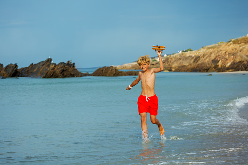 Young boy run holding toy model of the plane on the ocean beach with feet in the water