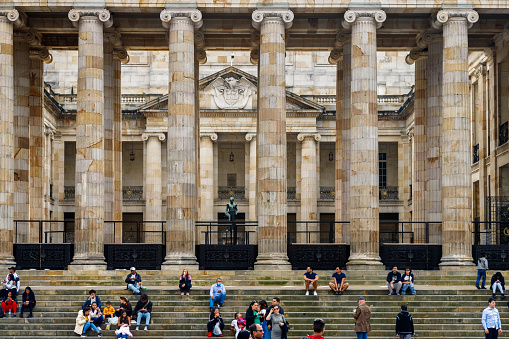 Bogota, Colombia - January 1, 2023: Dozens of tourists sit on the steps of the National Capitol in Plaza Bolivar, the main square of Bogota