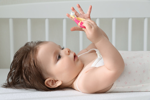 Cute little baby with toothbrush in comfortable crib at home