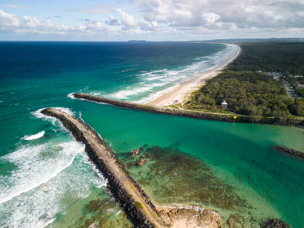 Aerial view of two rocky jetties and pristine beach with coastal forest Drone view of rocky jetties and beach around them. Endless beach with clear blue ocean and white sandy beaches. Green coastal forest meets the wide sandy beach. Large white waves washing to the shore. jetty aerial stock pictures, royalty-free photos & images