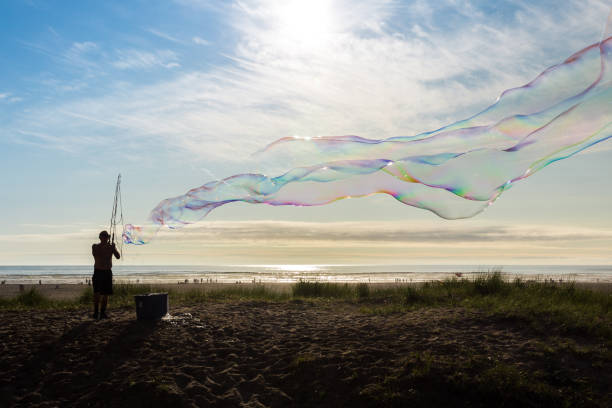 Seaside, Oregon, USA - July 16th, 2021: Silhouetted man creates huge soap bubbles on the beach