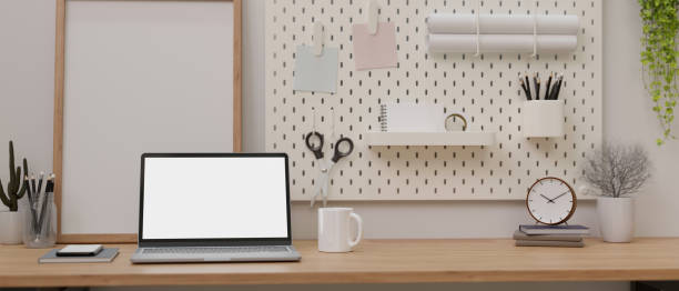istock A laptop white screen mockup on a wooden table against the wall with white pegboard. 1496002695