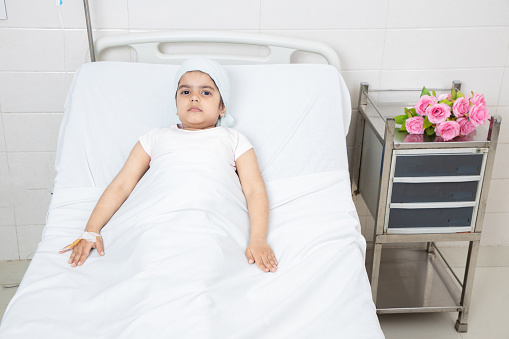 Smiling little girl child patient lying at hospital bed undergoing course of chemotherapy. Healthcare concept.