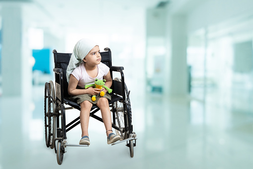 Young indian handicapped girl kid sitting on a wheelchair at hospital. Healthcare concept. Copy space