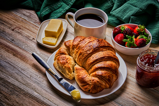 Food theme series: Breakfast with cup of coffee, croissants, marmalade, and fruits on wooden table