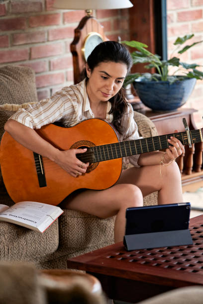 istock Hispanic beautiful young woman playing guitar with digital tablet, learn to play with an online course. 1496005478
