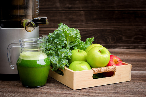 Fresh vegan green smoothie juice with kale vegetables and apple fruit on wooden desk background