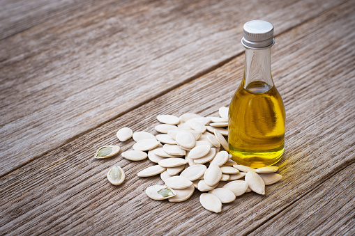 Pumpkin seed oil in glass bottle and dried pumpkinseed isolated on wooden table background.