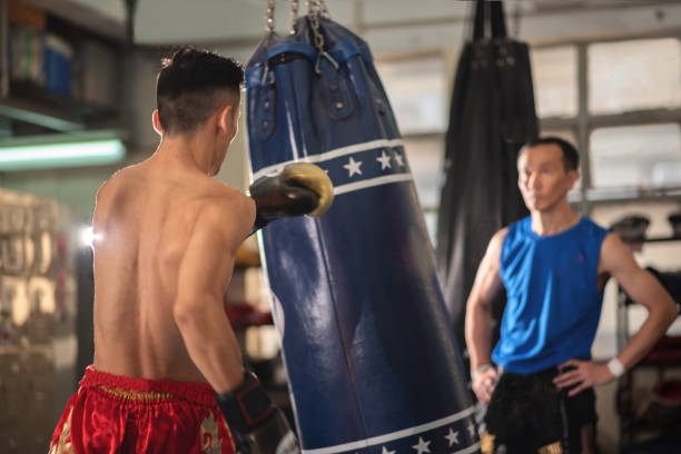istock Asian male boxer hitting a huge punching bag in front of instructor in boxer training. 1496025596