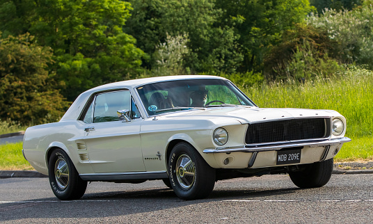Stony Stratford,UK - June 4th 2023: 1967 white FORD MUSTANG classic car travelling on an English country road.